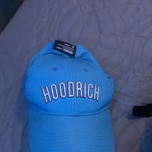 Blå keps från Hoodrich - Snygg blå keps från Hoodrich med broderad logga framtill. Kepsen är tillverkad i polyester och elastan för en bekväm passform. Perfekt för en avslappnad stil. Och köpt från JD och tror jag köpte den för 400-500 kr. Vill bara bli av med den har tröttnat 