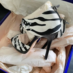 Zebramönstrade klackskor från Jimmy Choo - Snygga zebramönstrade klackskor från Jimmy Choo med dragkedja bak och dekorerade med glittriga stenar. Perfekta för att sticka ut på festen!