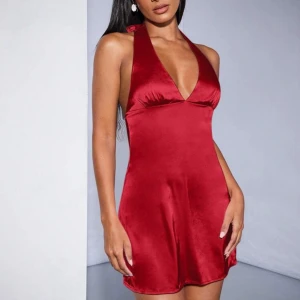 Röd axelbandslös klänning - Snygg röd klänning i satin med öppen rygg och knytband i nacken. Perfekt för en kväll ute eller en speciell tillställning. Den har en kort längd och en elegant passform. Helt ny 