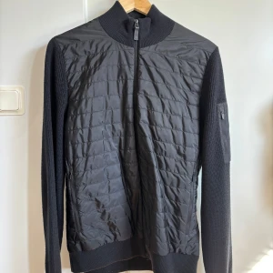 J.Lindeberg Cardigan Svart Medium - Svart snygg J.Lindeberg cardigan i modellen beck knitted hybrid jacket, knappast använd och perfekt nu till de soligare dagarna! Storlek medium, skriv för mer funderingar! 