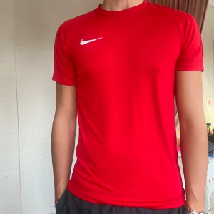 Röd Nike Träningströja - Snygg röd t-shirt från Nike med korta ärmar och en vit logga på bröstet. 