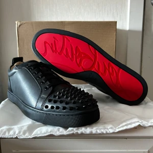 Christian Louboutin läder - Snygga svarta sneakers från Christian Louboutin med ikonisk röd sula och nitar på tån. Skorna har snörning och är tillverkade i skinn, vilket ger en lyxig känsla. Perfekta för att ge din stil en edgy touch.