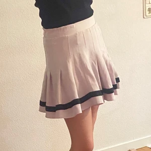 Beige kortkjol med svarta detaljer Från BERSHKA - Snygg beige kortkjol med svarta ränder längst ner. Kjolen har en veckad design som ger en fin volym och rörelse. Perfekt för en stilren och chic look. Från bershka och har använts flertal gånger men är inte sönder heller smutsig och kan användas mer.