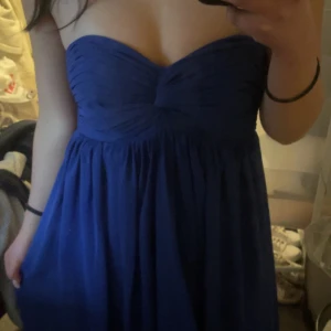 Blå axelbandslös balklänning - Säljer en elegant blå axelbandslös klänning med draperad detalj vid bysten. Perfekt för festliga tillfällen. Klänningen har en smickrande passform och ett flödande tyg som ger en vacker siluett.