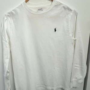 Vit långärmad tröja från Polo Ralph Lauren - Säljer en klassisk vit långärmad tröja från Polo Ralph Lauren. Tröjan har en rund halsringning och det ikoniska broderade logotypen på bröstet. Perfekt för en stilren och avslappnad look.