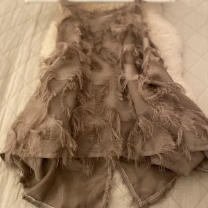  Söta topp med fransar - Säljer en  beige top med fransdetaljer som ger en cool textur. Klänningen har en lös passform och är ärmlös, perfekt för en trendig look. Den är gjord i ett lätt material som ger en luftig känsla.