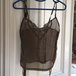 Brun transparent linne med spetsdetaljer - Säljer ett elegant brunt transparent linne med justerbara axelband och vacker spetsdetalj vid halsringningen. Perfekt för en stilfull look.