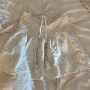 Vit kjol från Zara - Säljer en söt vit kjol från Zara med fina broderings detaljer och knytband med pärlor och tofsar. Kjolen har en elastisk midja och är perfekt för varma dagar. Aldrig använd!💕