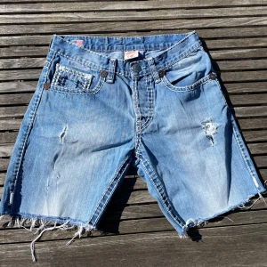 Big stitch True religion Shorts - Säljer ett par big stitch true religion shorts i storlek 31.  De har en snygg fade och med slitningar. Detta är ett sällsyntare par med den Amerikanska flaggan vilket betyder att det är Made In USA. Säljer tyvär de billigare för de är avklippta till shorts. Bara medela om du har frågor eller vill ha mått!