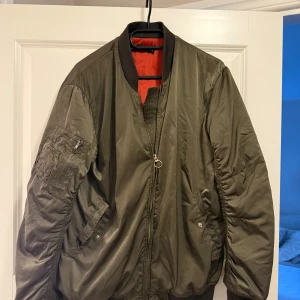 Olivgrön bomberjacka med orange foder - Säljer en klassisk olivgrön bomberjacka från Zara  med orange foder. Hål i ena fickan storlek L men mer som en M