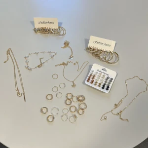 Smyckeset i guld och pärlor från Fashion Jewelry - Ett elegant smyckeset från Fashion Jewelry med guldpläterade örhängen, armband och halsband. Setet inkluderar flera ringar, pärlörhängen och hoops i olika storlekar. Perfekt för att mixa och matcha för olika stilar. (35kr per styck)