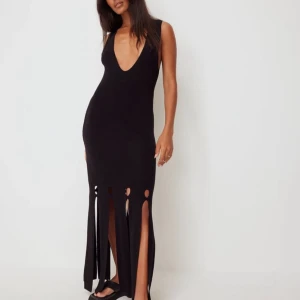 Svart ärmlös klänning med öppen rygg - Snygg svart långklänning med djup v-ringning och öppen rygg. Klänningen har slitsdetaljer nertill och knytband i ryggen för en elegant look.