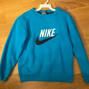 Blå sweatshirt från Nike - Blå  sweatshirt från Nike med klassisk logga i vitt och svart framtill. Tröjan har rund halsringning, långa ärmar och ribbade muddar vid ärmslut och nederkant. Perfekt för en sportig och avslappnad stil. Passar XXS/XS, superfint skick.