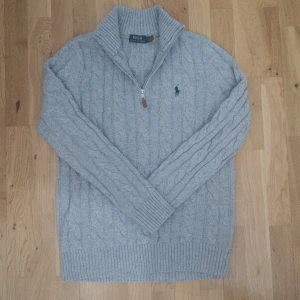 Grå kabelstickad halv zip från Ralph Lauren - Säljer en klassisk grå kabelstickad tröja från Polo Ralph Lauren med halv dragkedja och hög krage. Tröjan är använd endast en gång då den var för liten för mig. Köpt från Zalando. Tar gärna byten så kom med förslag :) Priset går att diskutera :) (inom rimlighetens gränser)
