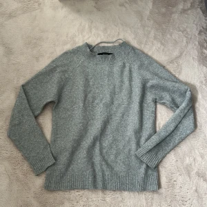 Ljusgrå stickad tröja från Vero Moda - Mysig ljusgrå stickad tröja från Vero Moda. Tröjan har rund halsringning, långa ärmar och ribbade muddar vid ärmslut och nederkant. Perfekt för lager-på-lager och enkel att matcha med olika outfits.
