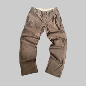 Bruna chinos från Puma - Säljer ett par bruna chinos från Puma med klassisk passform och diskret Puma-logga på fickan. Byxorna har bälteshällor, dragkedja och knäppning framtill samt två bakfickor. Perfekta för en stilren och avslappnad look.