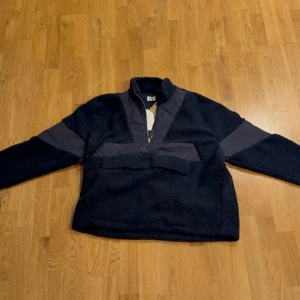 Svart fleecejacka half zip från Pier One - Mysig svart fleecejacka från Pier One med halv dragkedja och mörka detaljer över bröst och armar. Jackan har hög krage och lång ärm, perfekt för kyliga dagar. Snygg och enkel design som passar till mycket.