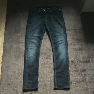 Säljer ett par mörkblå slim fit jeans från Replay. Klassisk femficksmodell med snygga slitningar och Replay-logga på bakfickan. Jeansen har normal midja och är tillverkade i stretchigt denim för en bekväm passform. Jeansen är i storlek 154 cm som motsvarar ungefär w26
