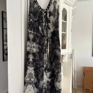 Svartvit långklänning med snörning från Mingel - Säljer en svartvit långklänning från Mingel med coolt abstrakt mönster. Klänningen har snörning framtill med metallöljetter och breda axelband. Perfekt för dig som vill sticka ut med en unik look.