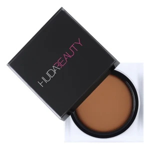 Huda Beauty Cream Bronzer - Krämig foundation från Huda Beauty i en snygg fyrkantig svart burk med transparent botten. Färgen är medium till mörkbrun och ger en jämn och naturlig finish. Perfekt för dig som vill ha en täckande bas med lyxig känsla.