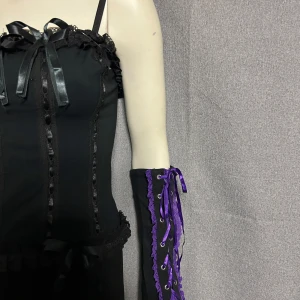 Svarta handskar med lila snörning - Unika svarta handskar med dekorativ lila snörning och spetsdetaljer. Perfekta för att ge en edgy touch till din outfit. Snörningen ger en justerbar passform och spetsen tillför en feminin känsla. Helt nya. Bomullstrikå.