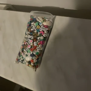Pärlor i blandade färger och former - En påse med blandade pärlor i olika färger och former, inklusive bokstavspärlor, siffror och hjärtan. Perfekt för att skapa egna smycken som armband eller halsband. Pärlorna är i plast och kommer i en återförslutningsbar påse.