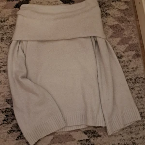 Beige offshoulder stickad tröja - Mysig beige stickad tröja med bred offshoulder-krage. Tröjan har långa ärmar och ribbade muddar vid ärmslut och nederkant. Perfekt för lager-på-lager och en chill look.