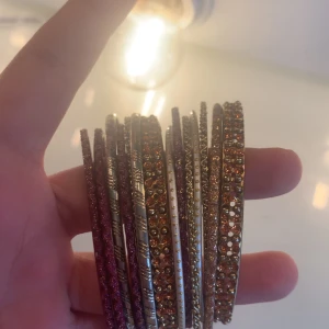 Set med glittriga armband i guld, rött och vitt - Säljer ett set med flera smala armband i olika färger och mönster. Armbanden är glittriga och har detaljer i guld, rött och vitt. Perfekta för att mixa och matcha för en personlig stil.