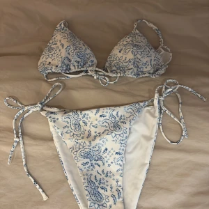 Vit och blå bikini från Gina Tricot - Superfin bikini från Gina Tricot i vitt med blått paisleymönster. Klassisk trekantsmodell upptill och knyt i både överdel och underdel för justerbar passform. Båda säljs tillsammans! (Aldrig använd)