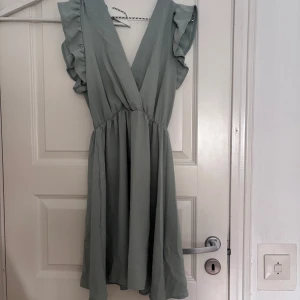 Omlottklänning - Superfin ljusgrön klänning med omlottliv och volangärmar. Klänningen har en v-ringad hals och resår i midjan samt knytning baktill. Köpt i Italien 💗