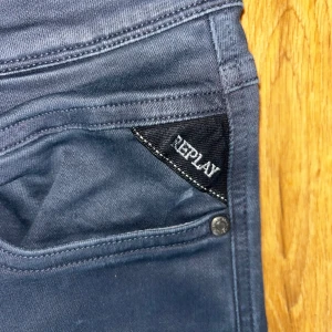 Mörkblå Replay jeans - Säljer ett par mörkblå jeansbyxor från Replay med klassisk femficksdesign och raka ben. Byxorna har svarta detaljer vid fickan och Replay-logga på bakfickan samt läderpatch i midjan. Perfekta för dig som gillar stilrena jeans!