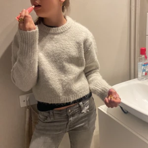 Ljusgrå stickad tröja från Zara - Mysig ljusgrå stickad tröja från Zara med rund halsringning och ribbade muddar. Tröjan har en croppad passform och långa ärmar, perfekt för lager-på-lager-stil. Enkel att matcha med både jeans och kjol.
