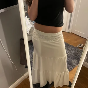 Vit långkjol från Gina Tricot - Säljer en vit långkjol från Gina Tricot med elastisk midja. Kjolen har en luftig och bekväm passform med flera lager som ger en fin volym. Perfekt för varma dagar och kan enkelt matchas med olika toppar.