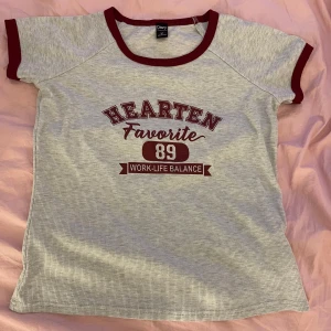 Grå och vinröd t-shirt med tryck - Grå t shirt med vinröda detaljer. Tryck på bröstet med texten 'HEARTEN Favorite 89 WORK-LIFE BALANCE' i vinrött. Klassisk passform och korta ärmar.