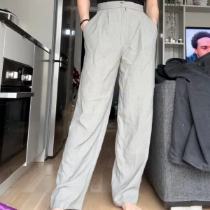 Gråvita kostymbyxor med smått rutigt mönster - OBS!! ALLA MINA PLAGG GRATIS VID UPPHÄTMNING I RÅCKSTA!!! Snygga gråvita kostymbyxor med diskret rutigt mönster och hög midja. Byxorna har vida ben, är gjorda i väldigt tunt och luftigt tyg. En knappt saknas, se bild 3. Köpta secondhand, skulle må bra av en ny fåll i benen. 