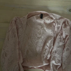 Ljusrosa spetsbolero - Säljer en ljusrosa bolerotopp i spets med lång ärm. Perfekt att ha över ett linne eller klänning för en extra touch. Tunt och genomskinligt material med vacker spetsstruktur.
