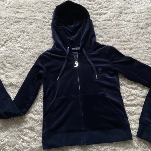 Mörkblå velour hoodie från Juicy Couture - Säljer en mörkblå zip hoodie från Juicy Couture. Jätteskönt material både utanpå och inuti! Denna tröjan passar till alla tillfällen, slappa dagar hemma men även till lite mer uppklädda tillfällen💞