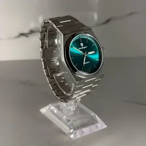 Snygg herrklocka med grön urtavla och dag/datumvisning. Klockan har en stilren silverfärgad länk i metall och kvartsverk. Perfekt accessoar för dig som gillar klassisk design med modern touch. BOX, ALLA LÄNKAR och LÄNKJUSTERARE MEDFÖLJER! PRISET KAN DISKUTERAS VID SNABB AFFÄR!
