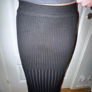 Svart ribbad långkjol - Säljer en svart ribbad långkjol. Kjolen är figurnära och har en stretchig passform som sitter snyggt längs kroppen. Perfekt att styla med en enkel topp eller stickad tröja.