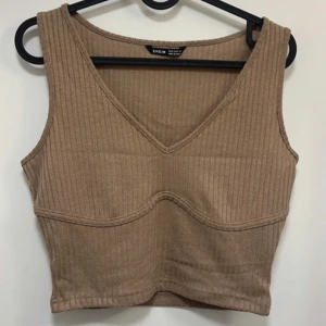 Beige ribbad croppad linnetopp från Shein - Säljer en beige ribbad croppad linnetopp från Shein med v-ringning. Toppen är ärmlös och har en figurnära passform, perfekt att styla till olika outfits.