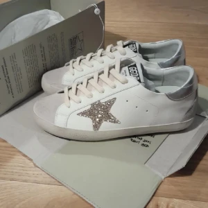 SÖKER!!  från Golden Goose - Söker! ett par vita sneakers från Golden Goose med beige detaljer och en glittrig stjärna på sidan. Skorna har silverfärgad häl och klassisk snörning. Perfekta för dig som vill ha något extra till vardagslooken. Kan köpa mellan 1000-2000kr, hör gärna av er om ni har ett par i fint skick (stolek 38)
