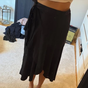 Svart omlottkjol med knytband - Svart omlottkjol med knytband i midjan och lätt utsvängd passform. 