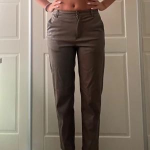 Bruna skinnbyxor med raka ben - Snygga bruna byxor i skinnimitation med raka ben och hög midja. Byxorna har fickor fram och bak, bälteshällor och stängs med dragkedja och knapp. Byxorna slutar vid anklarna. Jag är 165 cm.