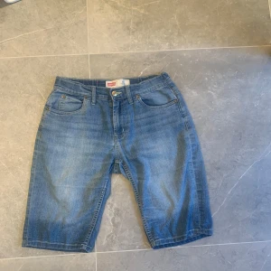 Levi's 511 blå jeansshorts slim - Klassiska blå jeansshorts från Levi's modell 511 Slim. De har fem fickor, bälteshällor och knappgylf. Snygg tvättad denim med normal passform och raka ben. Perfekta för en chill sommarstil.