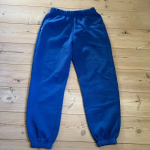 Blå mjukisbyxor med resår - Snygga blå mjukisbyxor med resår i midjan och vid bensluten. Byxorna har sidofickor och är gjorda i mjukt bomullsmaterial, perfekta för chill eller träning. Enkel och clean design som passar till allt.