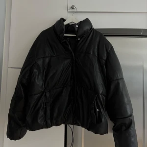 Svart pufferjacka från Vero Moda - Säljer en svart pufferjacka från Vero Moda i storlek L. Jackan har en cool oversized passform, hög krage med tryckknappar framtill. Jackan är i skinnimitation
