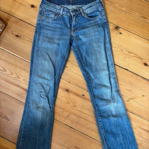 Blå bootcut jeans från Seven For All Mankind - Snygga blå jeans från Seven For All Mankind i klassisk bootcut-modell. Jeansen har fem fickor, orange sömmar och är tillverkade i stretchig denim med 98% bomull och 2% polyuretan. Storlek 26 i midjan och skulle säga en 32 i längden så passar mig som är 167cm men skulle även passa lite längre/kortare. Så snygga gamla favoritjeans & köpta här på Plick för 600 men använder knappt längre!🩷