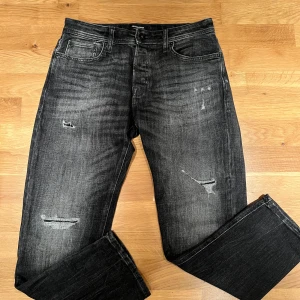 Svarta tapered jeans Jack & Jones - Snygga svarta jeans från Jack & Jones i modellen Tapered/Mike. Jeansen har slitna detaljer och en tvättad look som ger en cool vibe. Klassisk femficksmodell och tillverkade i mjukt denimtyg. Perfekta för dig som gillar en avslappnad men trendig stil.