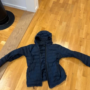Mörkblå dunjacka Peak Performance M - Snygg mörkblå dunjacka från Peak Performance i storlek M. Jackan har huva, dragkedja framtill och två sidofickor med dragkedja. Quiltad design och diskret logga på bröstet. Perfekt för kyliga dagar och har en sportig vibe.