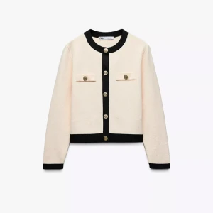 Beige kofta med svarta detaljer från Zara - Snygg beige kofta från Zara med svarta kontrastdetaljer vid krage, knappslå och muddar. Guldknappar framtill. Har används fåtal gånger men ser ut som ny. 